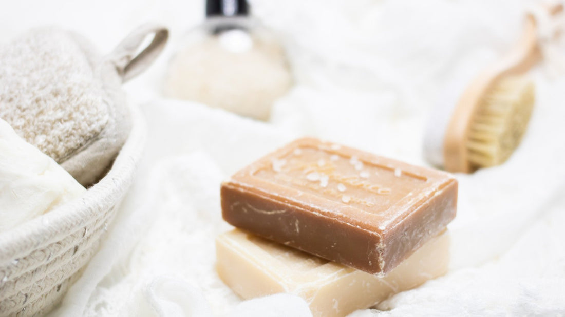 Bar soaps, a bath brush and skincare items on a white towel
